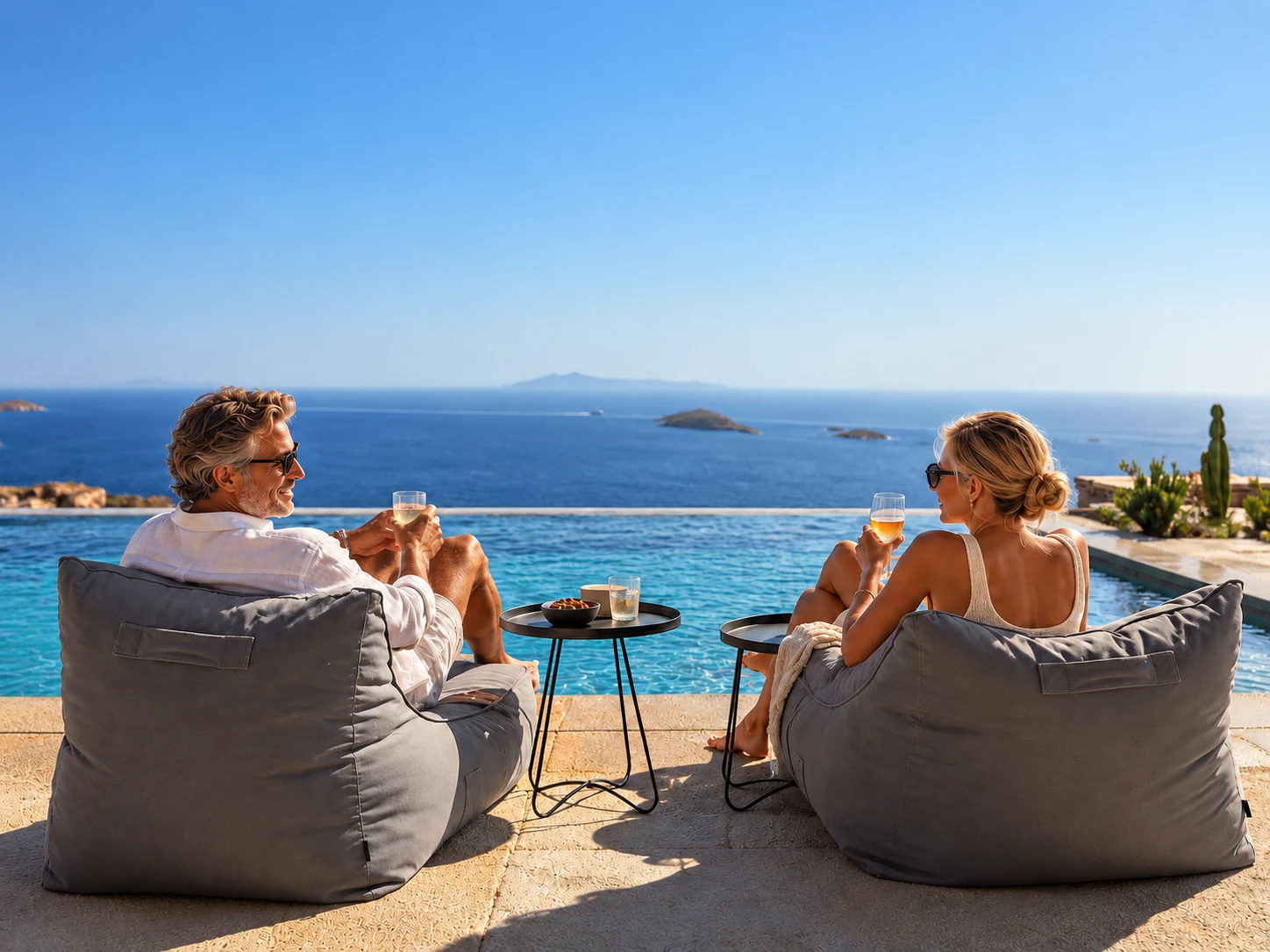A couple sharing drinks beside the infinity pool with Aegean views